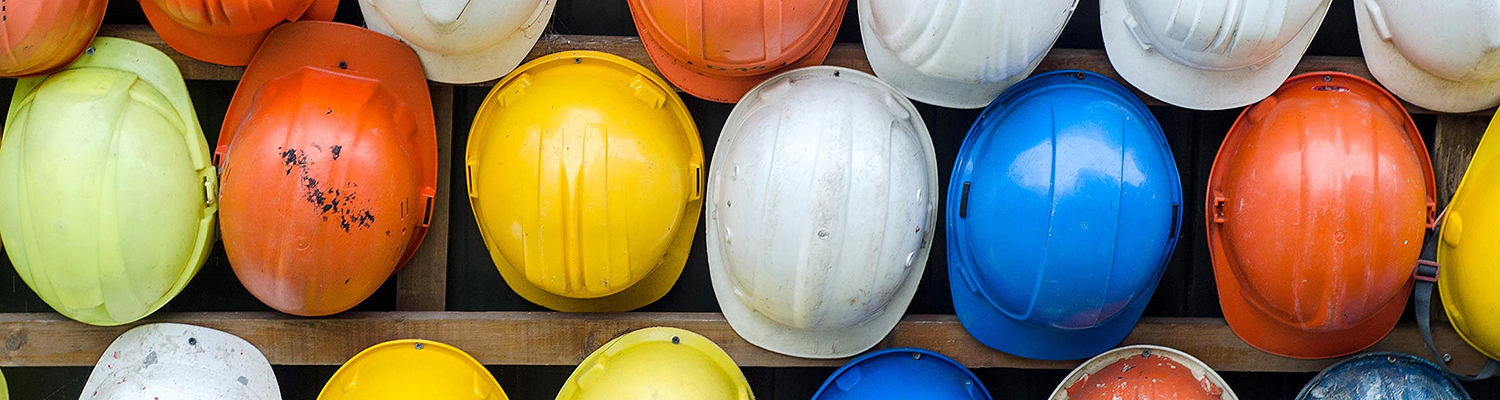 Hard hats in variety of colors hanging on wall.